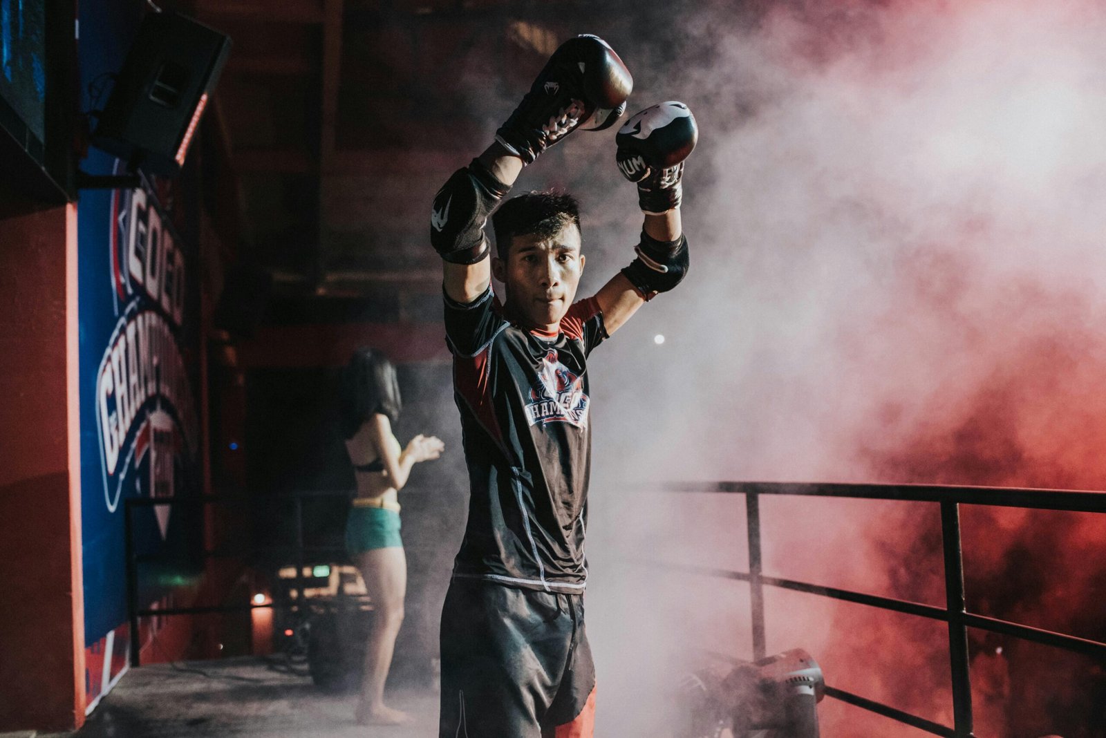 Boxer in dramatic lighting raises arms in victory before a match.