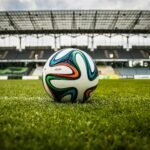 A vibrant soccer ball rests on a lush green field inside an empty stadium, capturing the essence of sports.