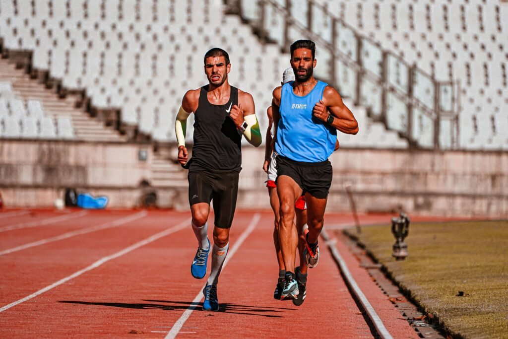 Two male runners competing on a stadium track during a sunny day.